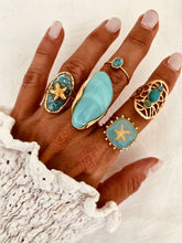 Učitaj sliku u preglednik galerije, Hand wearing multiple turquoise and gold rings with starfish designs on a textured white background