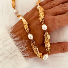 Load image into Gallery viewer, Freshwater pearl necklace displayed in the hand showcasing sculptural gold elements crafted from stainless steel with real gold plating.