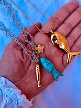 Load image into Gallery viewer, Gold fish pendant necklace displayed alongside turquoise and starfish necklaces in a coastal-inspired styling.