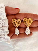 Učitaj sliku u preglednik galerije, NIKA statement earrings featuring textured gold hearts paired with elegant baroque pearl drops displayed on the hand.