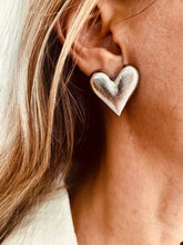Load image into Gallery viewer, Oversized silver heart statement earring worn on the ear, showcasing its bold sculptural design and brushed metallic finish.