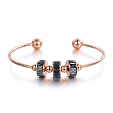 Load image into Gallery viewer, Close-up of bangle bracelet showing black and white roller elements with gold bead accents