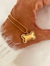 Load image into Gallery viewer, AKIKO gold dog bone necklace displayed on the hand, featuring a polished dog bone pendant surrounded by sparkling zircon stones on a delicate gold chain.
