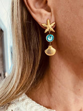 Load image into Gallery viewer, Gold earrings with a starfish and shell worn on a model.
