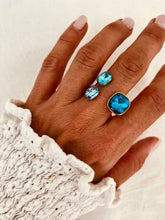 Load image into Gallery viewer, Gold plated stainless steel ring featuring a brilliant blue crystal on a woman's hand

