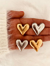 Load image into Gallery viewer, Gold and silver heart statement earrings displayed together, comparing both colour options with oversized sculptural heart shapes.
