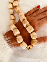 Load image into Gallery viewer, IZZA Cream Marble necklace photographed on the hand, featuring chunky marbled resin beads with polished gold spacer beads and a bold gold centre bead.

