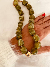 Load image into Gallery viewer, IZZA Olive Marble statement necklace displayed on the hand with rich olive green marbled resin beads and polished gold accents.
