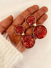 Load image into Gallery viewer, NYOKO red resin statement earrings displayed in a hand, showing the shimmering textured resin finish and elegant gold frame.
