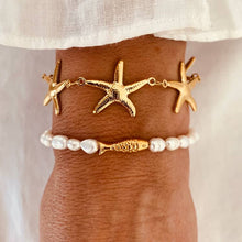 Load image into Gallery viewer, Gold starfish bracelet worn on wrist styled with summer outfit for elegant beach inspired look
