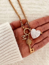 Load image into Gallery viewer, Close-up of the MIA personalized charm necklace showcasing the carved white heart, gold key and custom initial on a chunky gold chain.
