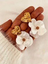 Load image into Gallery viewer, Pair of YNES white flower earrings displayed flat, showcasing the detailed resin petals, textured gold heart and polished stainless steel post.
