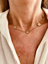 Load image into Gallery viewer, Gold flower charm necklace worn on model styled with light summer outfit showing feminine and elegant appeal
