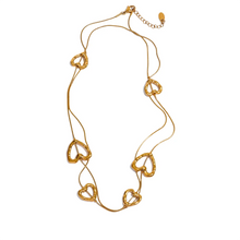 Load image into Gallery viewer, Long gold stainless steel heart charm necklace with small delicate heart details along the chain 
